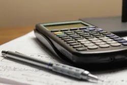 une calculatrice et un stylo posés sur un cahier contenant des calculs écrits à l'intérieur