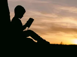 La silhouette d'un enfant qui lit la Bible devant un coucher de soleil en arrière-plan