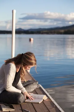Une fille lit la Bible à côté d'un lac dur un dock