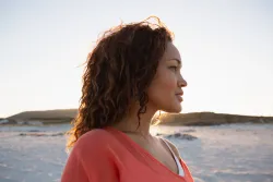 Vue latérale d'une belle femme métisse regardant au loin sur la plage
