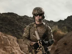 un soldat tenant une arme avec un terrain vallonné brun en arrière-plan